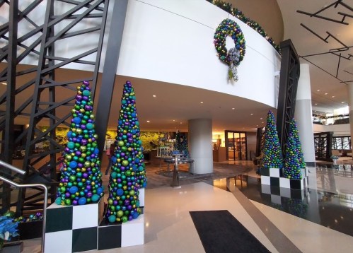 Decorated lobby with colorful Christmas trees and a festive wreath, featuring blue, green, and purple ornaments.