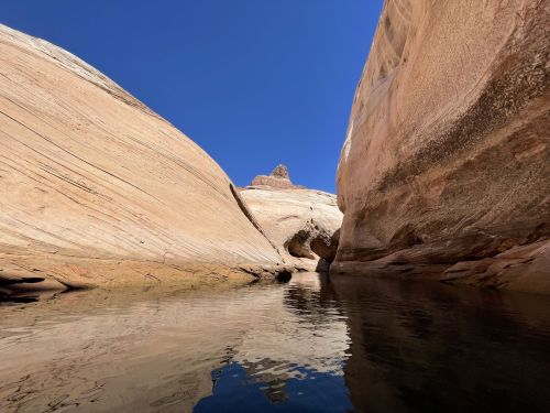 A serene canyon with smooth, layered rock formations and a calm water reflection under a clear blue sky.