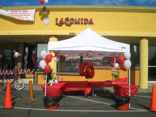 A festive outdoor setup with a white tent, red balloons, and tables decorated for an event outside a restaurant.