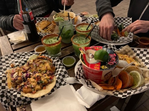 A table filled with various tacos, drinks in jars, and sides, all served on checkered paper.
