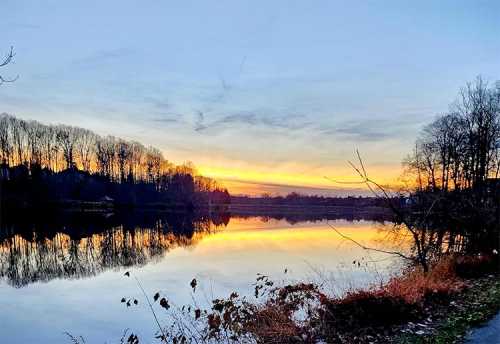 A serene lake at sunset, reflecting vibrant colors and silhouetted trees along the shore.