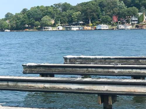 A view of a calm lake with wooden docks in the foreground and houses along the shore in the background.