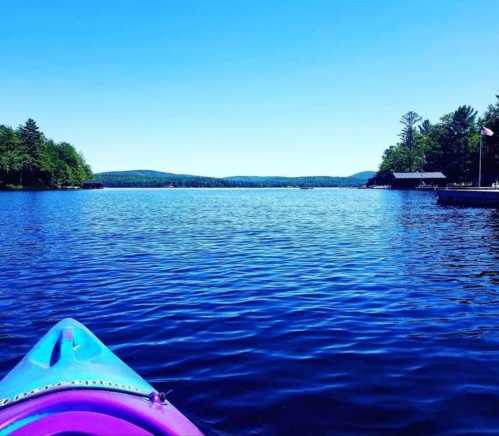 A colorful kayak on calm water, surrounded by trees and distant hills under a clear blue sky.