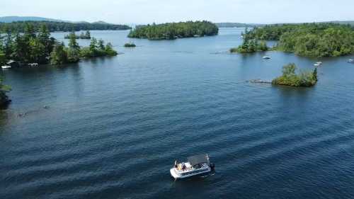 Aerial view of a boat on a calm lake surrounded by lush green islands and trees under a clear blue sky.