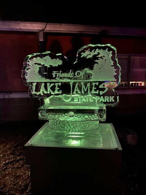 An illuminated ice sculpture featuring the text "Friends of Lake James State Park" against a dark background.
