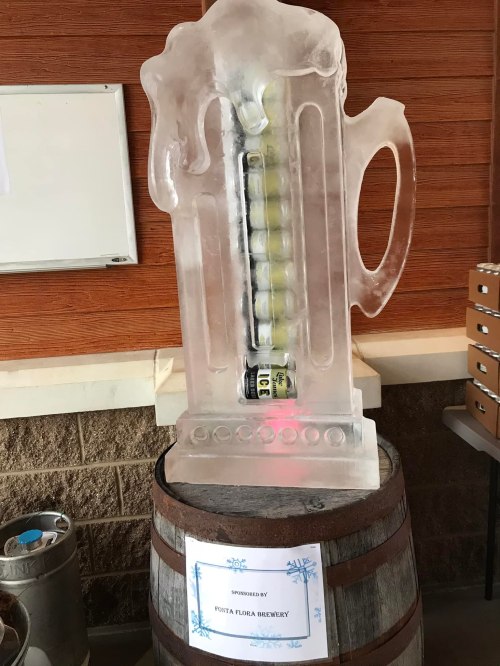 An ice sculpture of a beer mug with a thermometer inside, displayed on a wooden barrel.