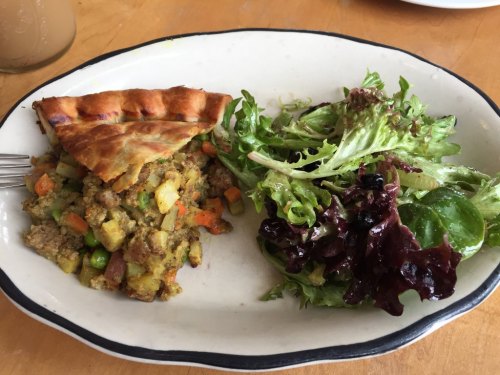 A slice of savory pie with mixed vegetables beside a fresh green salad on a white plate.