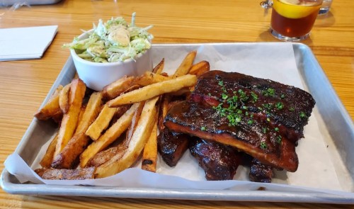 A tray with BBQ ribs, crispy fries, and a side of coleslaw on a wooden table.