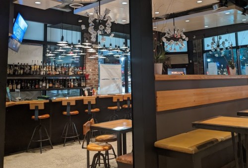 A modern restaurant interior featuring a bar with stools, wooden accents, and stylish lighting fixtures.
