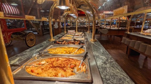 A buffet with various dishes displayed in metal trays under warming lamps on a marble countertop.