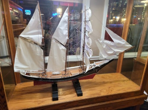 A detailed model of a sailing ship with white sails displayed in a glass case on a wooden base.