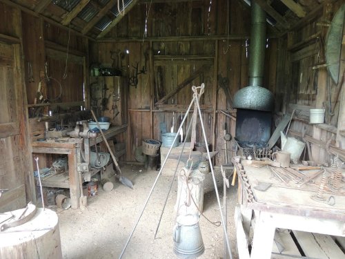 A rustic workshop with wooden walls, tools, a forge, and various equipment scattered around.