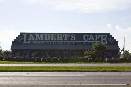 Sign for Lambert's Cafe, featuring large text and a blue sky in the background, with greenery in the foreground.