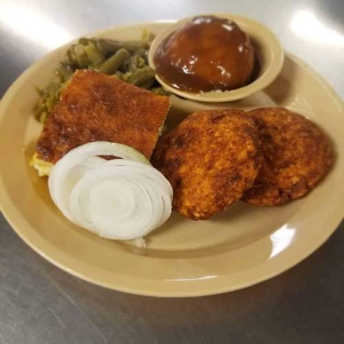 A plate with fried patties, sliced onions, green beans, cornbread, and a small bowl of dessert.
