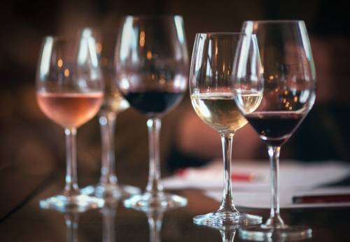 Five wine glasses filled with different types of wine, including rosé, white, and red, on a table.