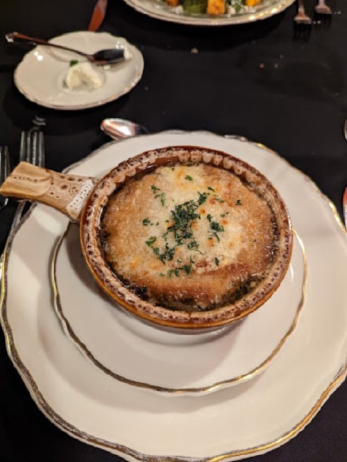 A bowl of French onion soup topped with melted cheese and herbs, served on an elegant plate.