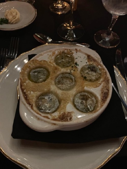 A dish of baked escargot in a creamy sauce, served in a white ceramic dish on a black napkin.
