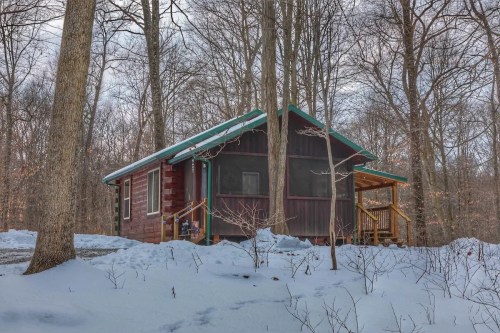 A cozy cabin nestled in a snowy forest, surrounded by bare trees and a clear winter sky.