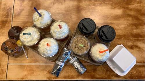 A variety of desserts and drinks, including milkshakes, cookies, and two cups with lids, arranged on a wooden table.