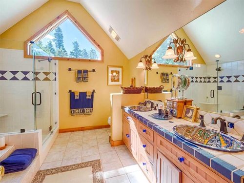 Bright bathroom with a double sink, colorful tile accents, a glass shower, and large windows letting in natural light.