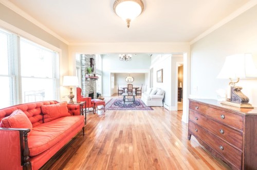 Bright living room with hardwood floors, red sofa, and elegant decor, leading to a dining area with a chandelier.