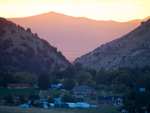 A serene valley at sunset, with mountains in the background and a small town nestled between the hills.
