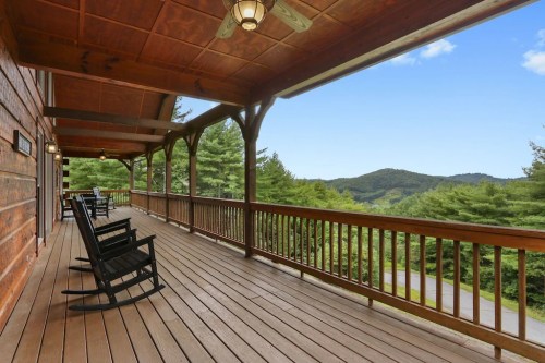 A wooden porch with rocking chairs overlooks a scenic mountain view under a clear blue sky.