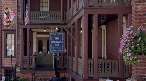Historic Maryland Inn with a sign, flags, and flower baskets, showcasing a charming architectural style.