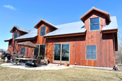 A modern wooden house with a metal roof, large windows, and a patio area on a sunny day.
