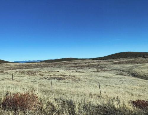 A vast, dry landscape with rolling hills under a clear blue sky and sparse vegetation.