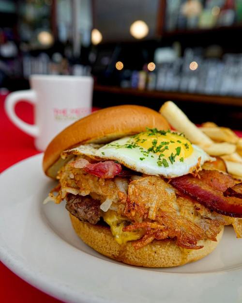 A hearty burger topped with bacon, a fried egg, and crispy hash browns, served with fries on a plate.