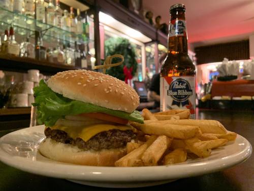 A juicy cheeseburger with lettuce and tomato, served with fries and a bottle of beer in a cozy bar setting.