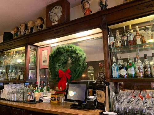 A wooden bar with a festive wreath, bottles of liquor, and a clock, creating a cozy atmosphere.