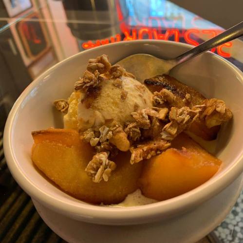 A bowl of dessert featuring sliced peaches, a scoop of ice cream, and a sprinkle of granola on top.
