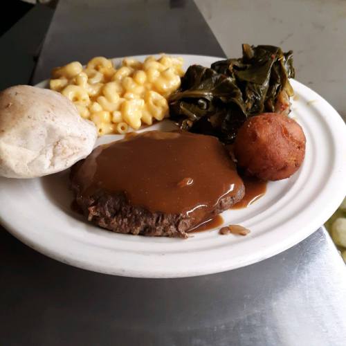 A plate of food featuring macaroni and cheese, collard greens, meatloaf with gravy, a biscuit, and a fried ball.