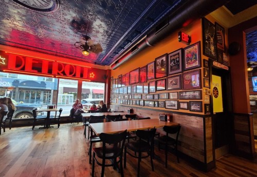 Interior of a restaurant with red lighting, wooden tables, and framed photos on the wall, featuring a view of the street outside.