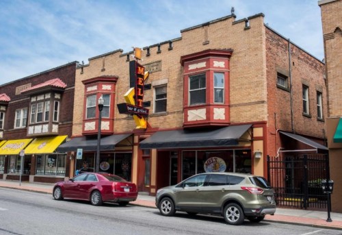 A street view of a brick building with a sign for "Melt," featuring parked cars and nearby shops.