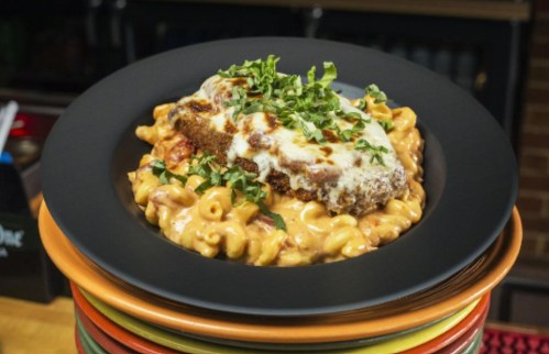 A plate of creamy macaroni and cheese topped with a breaded chicken cutlet and fresh herbs.