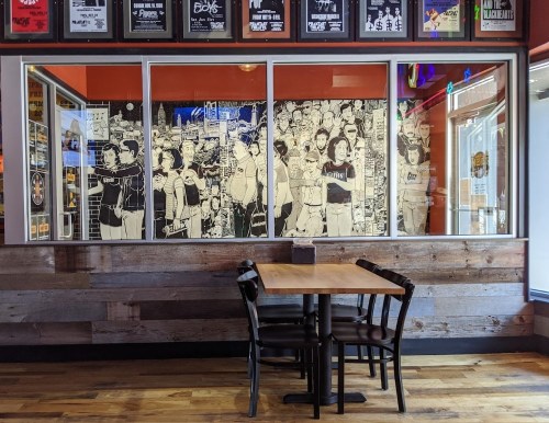 A wooden table with four chairs in front of a large mural featuring various people in a lively, illustrated style.