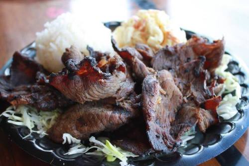 A plate of grilled meat served with rice, macaroni salad, and shredded lettuce.
