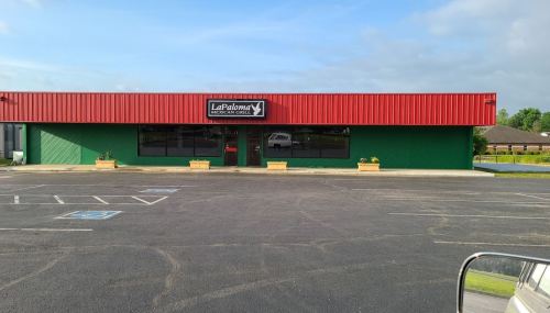 A green building with a red roof and sign reading "La Paloma" in a mostly empty parking lot.
