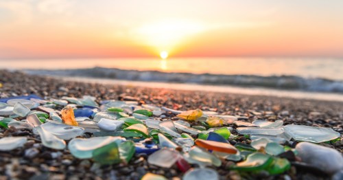 A pile of sea glass on a beach with the sunset in the background.