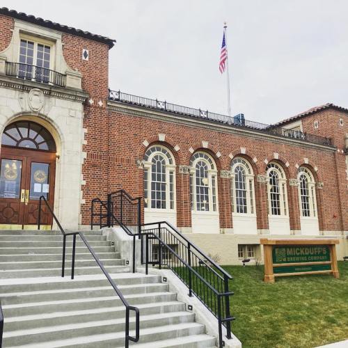 Historic brick building with large arched windows, stairs leading up, and an American flag flying above.