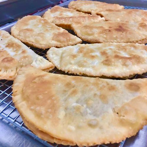 A tray of golden-brown fried pastries, some folded and others flat, cooling on a wire rack.