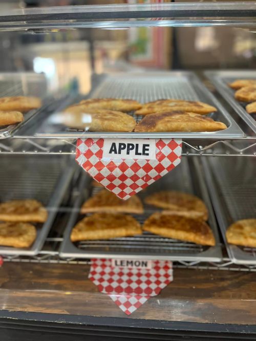 Baked pastries labeled "Apple" and "Lemon" displayed in a bakery case with a checkered pattern.