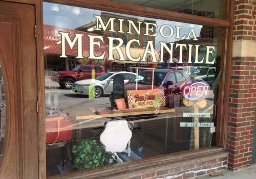 A storefront window displaying "Mineola Mercantile" with an "Open" sign and various items inside.