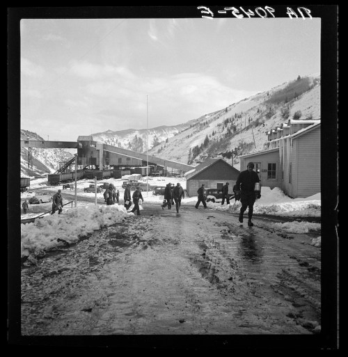 Workers walking through a snowy landscape near a mining facility, with mountains in the background.