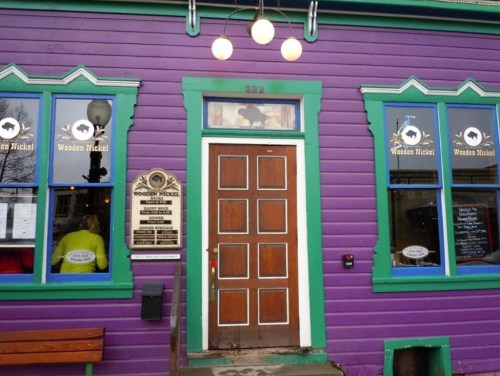 A vibrant purple building with green trim, featuring a wooden door and a sign for "Wooden Nickel."