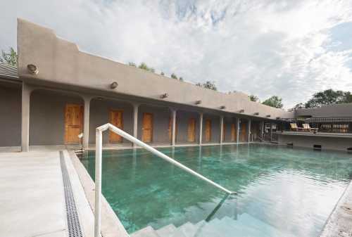 A serene pool area with a modern design, featuring doors along a wall and cloudy skies above.