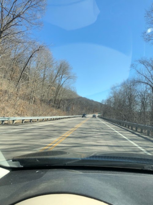 A view of a winding road with trees on the side, under a clear blue sky, as seen from inside a car.